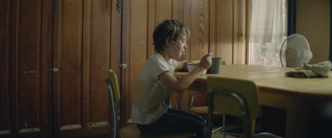 A kid is sitting at the kitchen table and eating breakfast