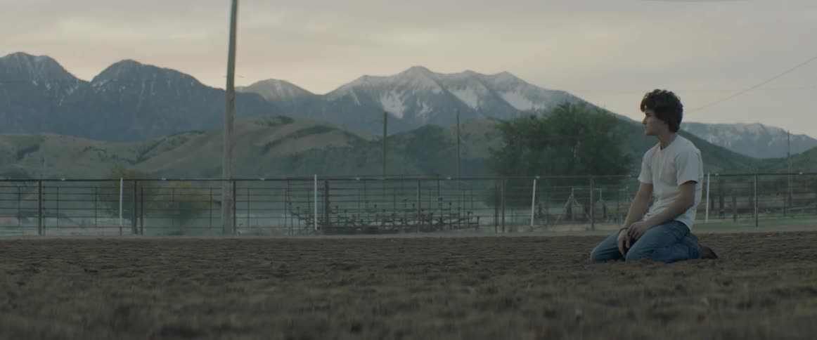 Young man kneels on the dirt in a corral