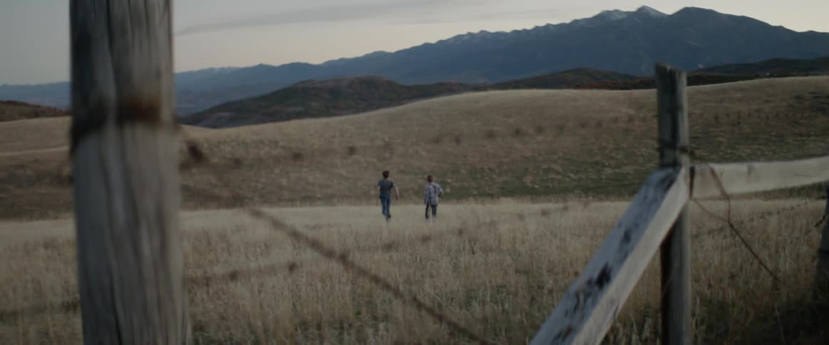 Boys run through a grassy field away from a fence
