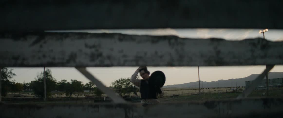 Young man carries a hat towards a fence