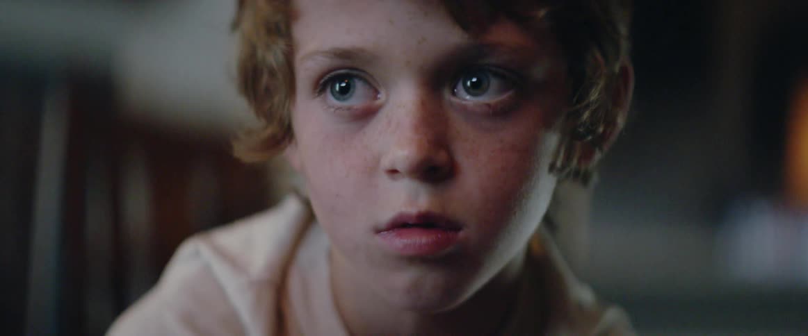 A young boy watches television in silence, absorbed by the shifting light
