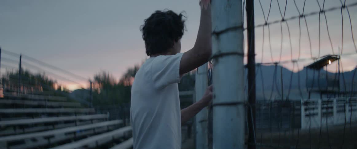 Man leans on a fence post near the bleachers