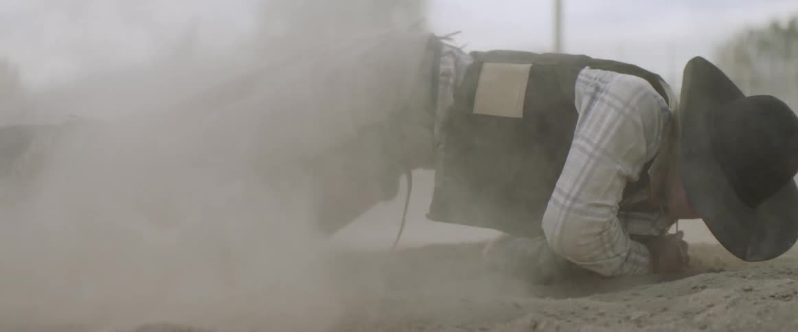 A cowboy lands in the sand and gets up to run