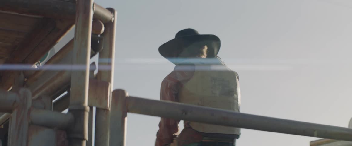 A man in a cowboy hat is sitting on a fence
