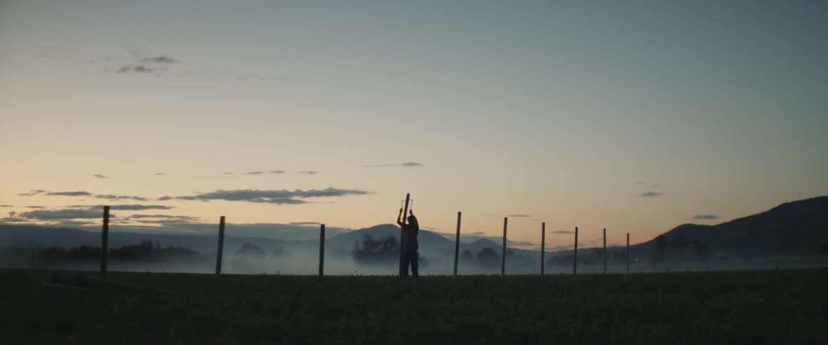 Man installs a fence on a ranch at sunset