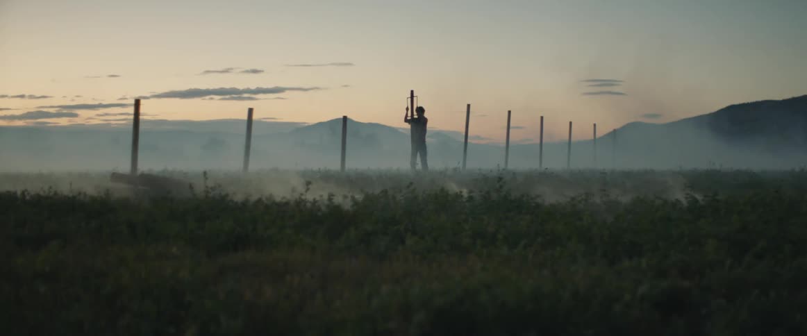 Man stands in a field, driving in a fence post