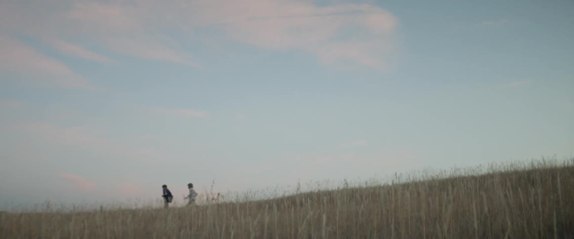 Boys run through a rural grassy field at sunset