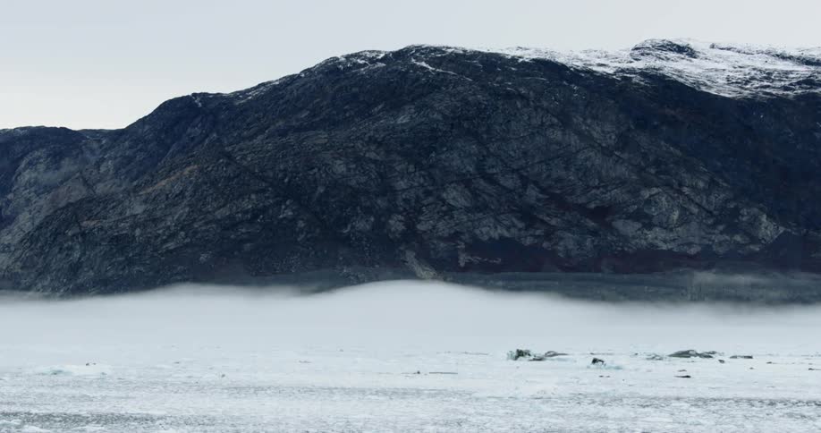 A large mountain is filmed from over the ocean by a drone