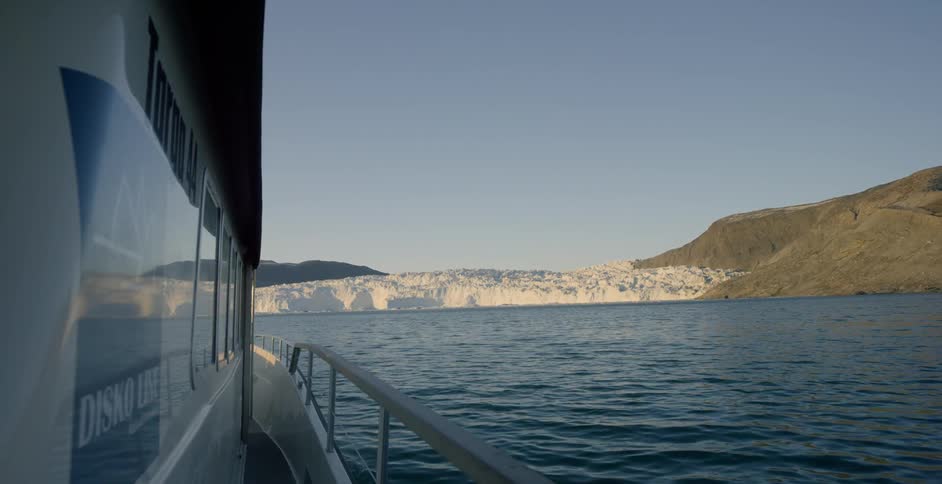 A ship is sailing toward a coastline with a glacier on a sunny day