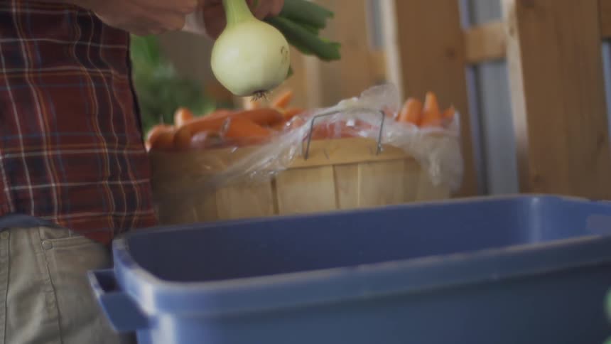 A man cuts the top from an onion and drops it into a bin of water