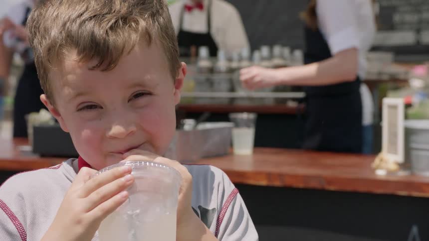 Boy drinks lemonade near a lemonade stand