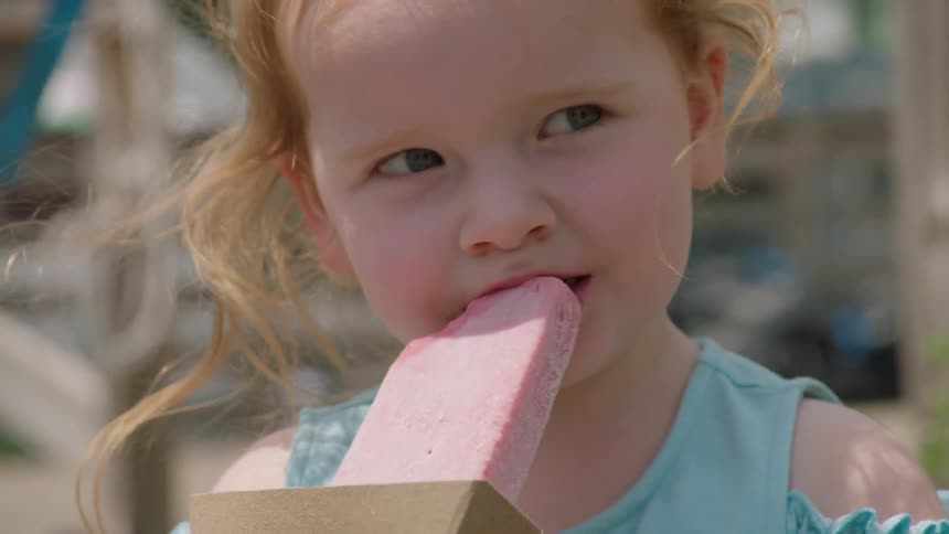 Little girl is smiling and eating ice cream outside on windy day