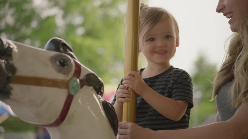 Little girl is smiling as she sits on carousel horse at fair