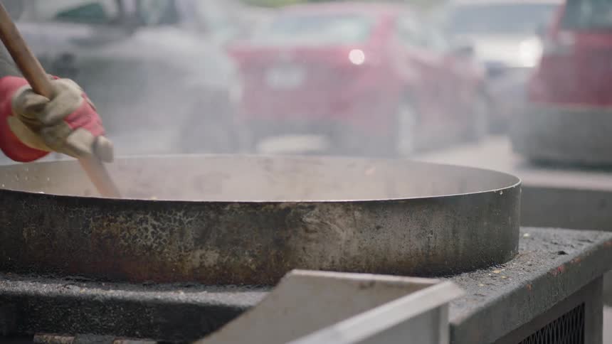 Someone stirs popcorn in a huge kettle