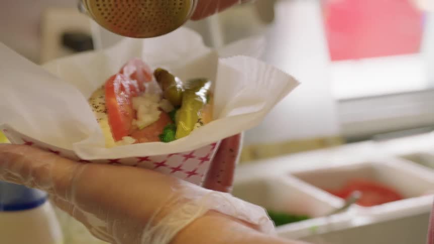Person in restaurant kitchen is putting toppings on hot dog