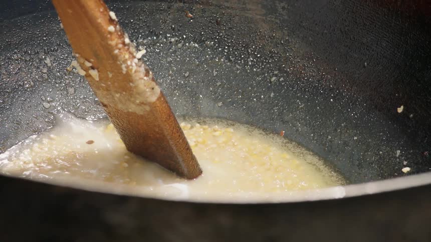Corn is being heated and stirred and sprinkled with salt in large pot