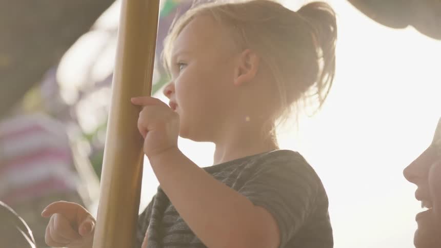 Little girl riding on carousel at fair is pointing and smiling