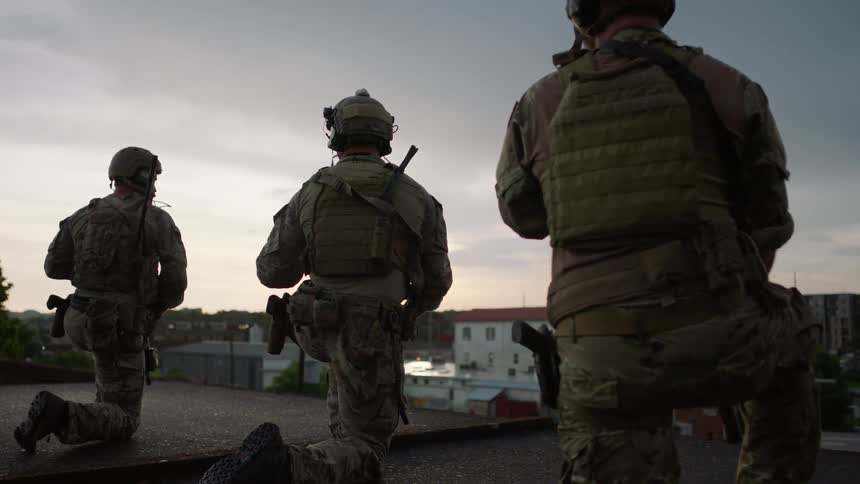 Soldiers kneel on a rooftop and scan the area