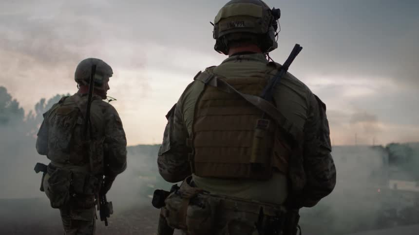Uniformed men holding guns stand outside with smoke billowing around