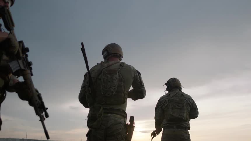 Uniformed men holding guns walk outside