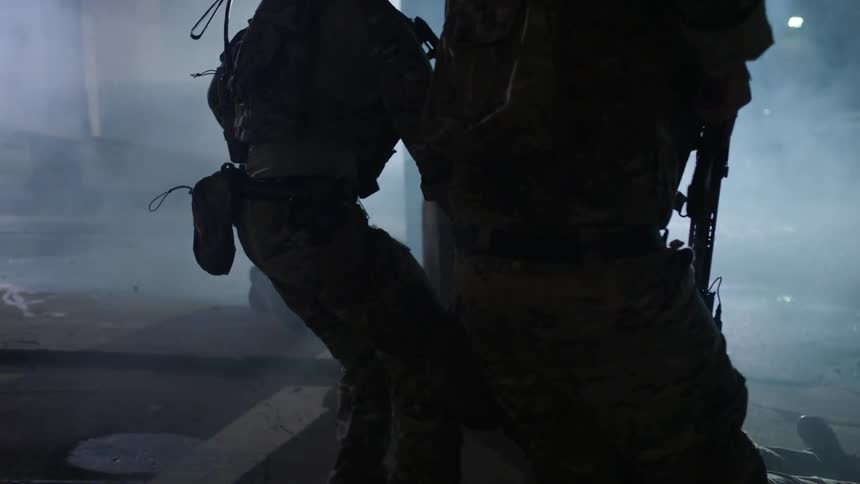 Soldiers dragging an injured soldier backwards while another covers them at night with lights shining