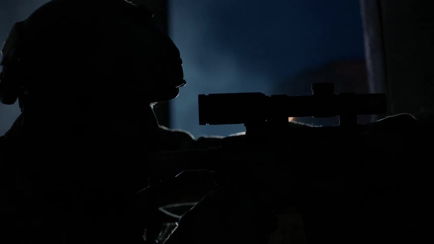 A sniper aims his rifle at night