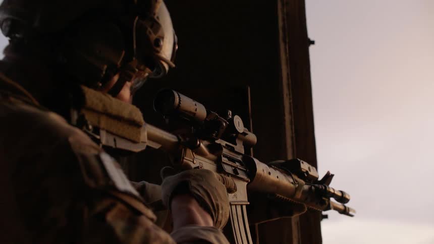 Soldier outside wearing helmet is aiming an automatic rifle