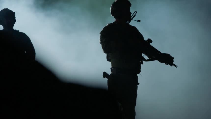 Soldiers walk across the smoke filled field with rifles