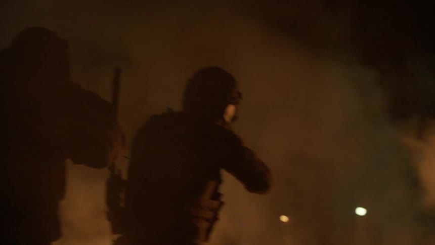 Soldiers walk through a fire and smoke filled area at night