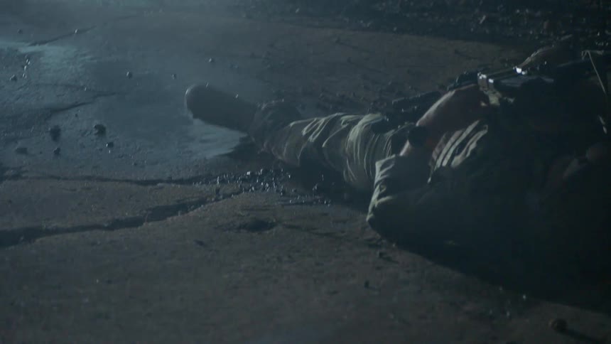 Soldier lying on the ground at night with others around him and lights flashing
