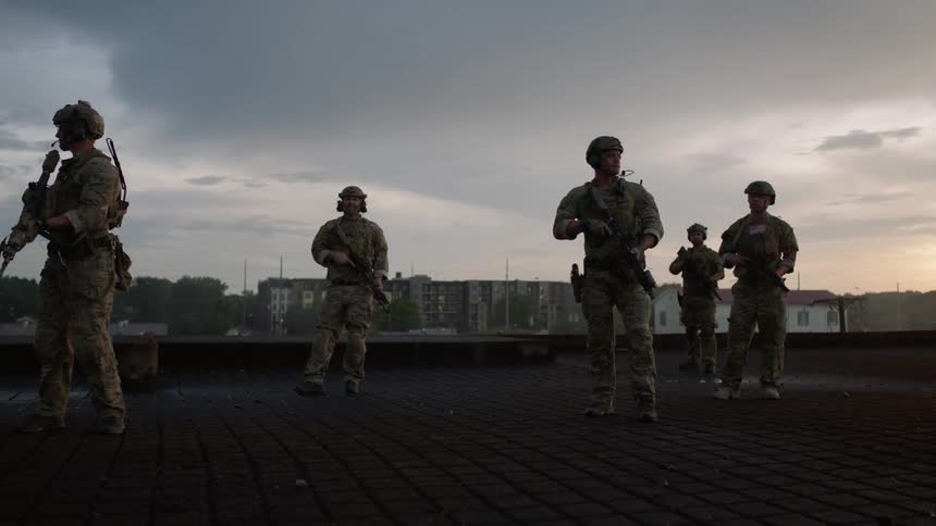Soldiers with weapons stand on a rooftop overlooking a city