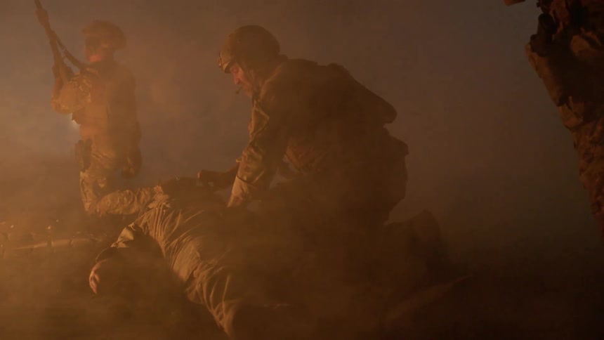 Soldiers in a smoky area at night while one is being tended to by another