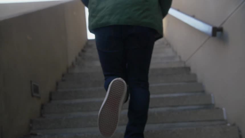 A view of someone's feet and legs as they run up a flight of concrete stairs