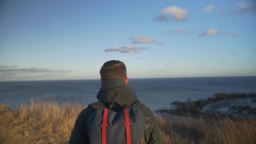 A man hikes towards an ocean side cliff at sunrise