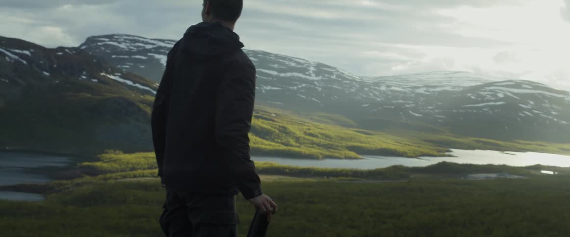 A man drinks from a thermos on a trail overlooking a mountain stream