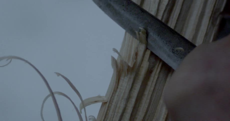 A man carves some wood off a log