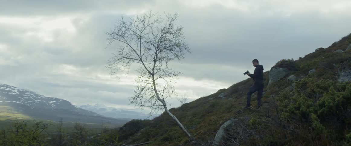 Man standing and taking photographs of mountains in wilderness on cloudy day