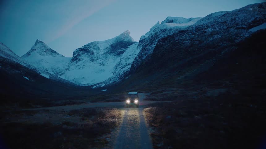Car traveling on dirt road in front of large snowy mountains at dusk