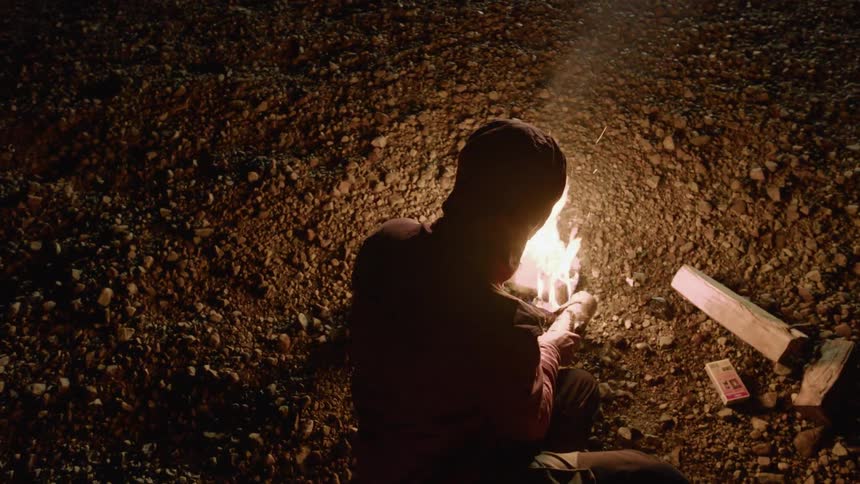 A man is building a campfire on the ground at night
