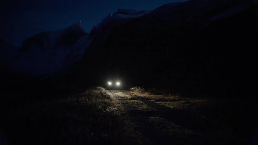 A car drives down a dirt road at night