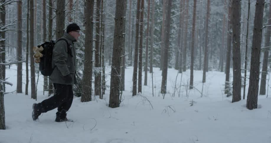 A man wearing a backpack walks through the woods in the snow