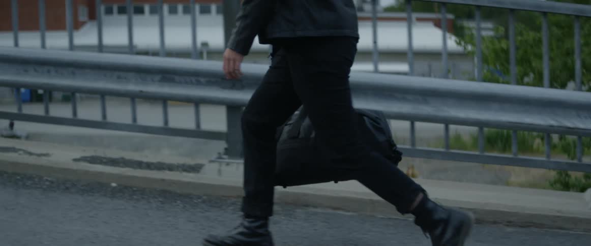 A man carrying a duffel bag walks over a city pedestrian bridge