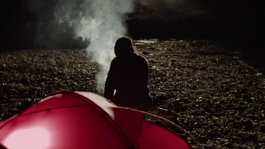 Man sits next to burning campfire and tent