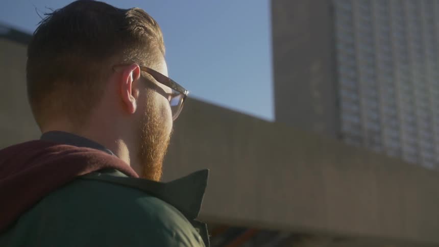 Young man wearing glasses walking down a city street on a sunny day