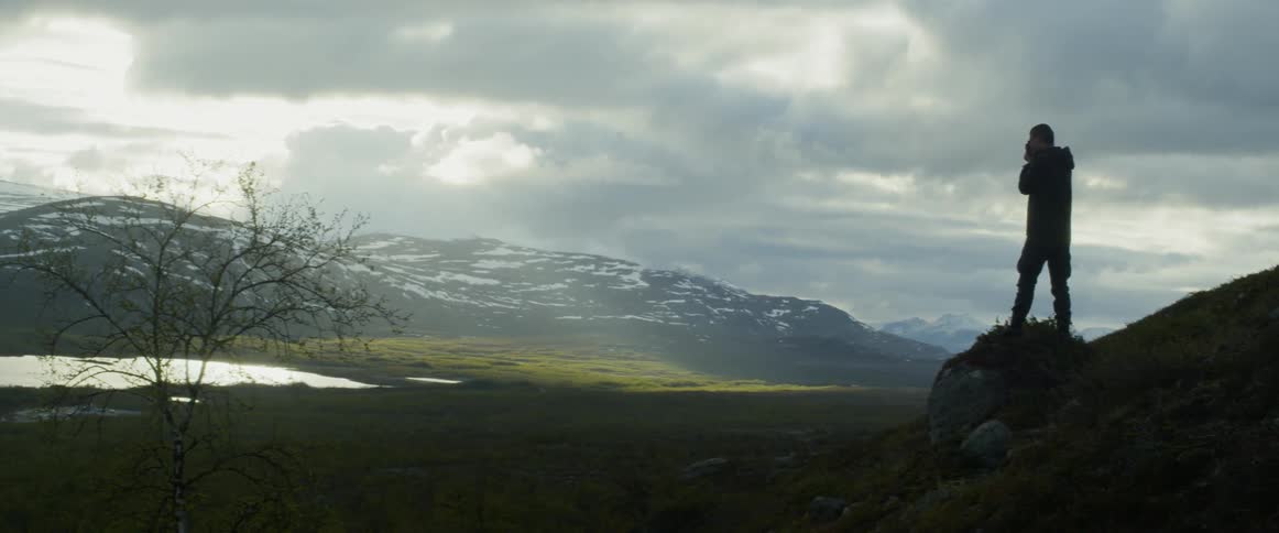 A man takes a photo of a lake near mountains on an overcast day