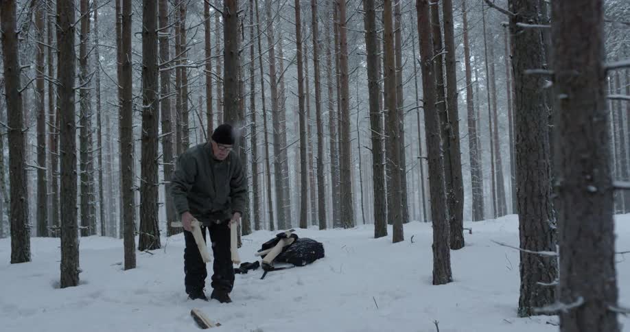 A man unpacks wood from a bag in a snowy forest