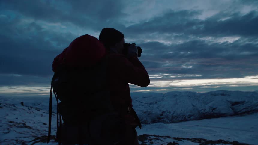 Hiker stands in snowy mountains at dusk