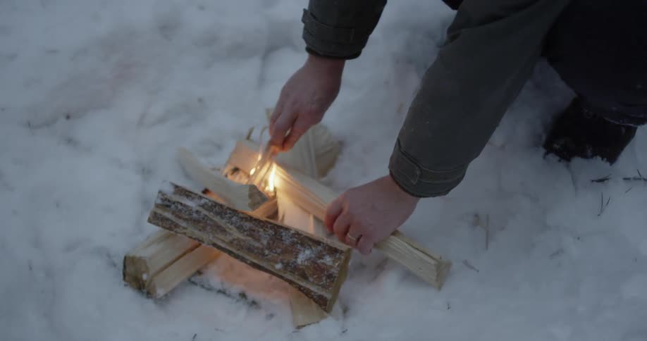 Person starting wood fire outside on snow covered ground