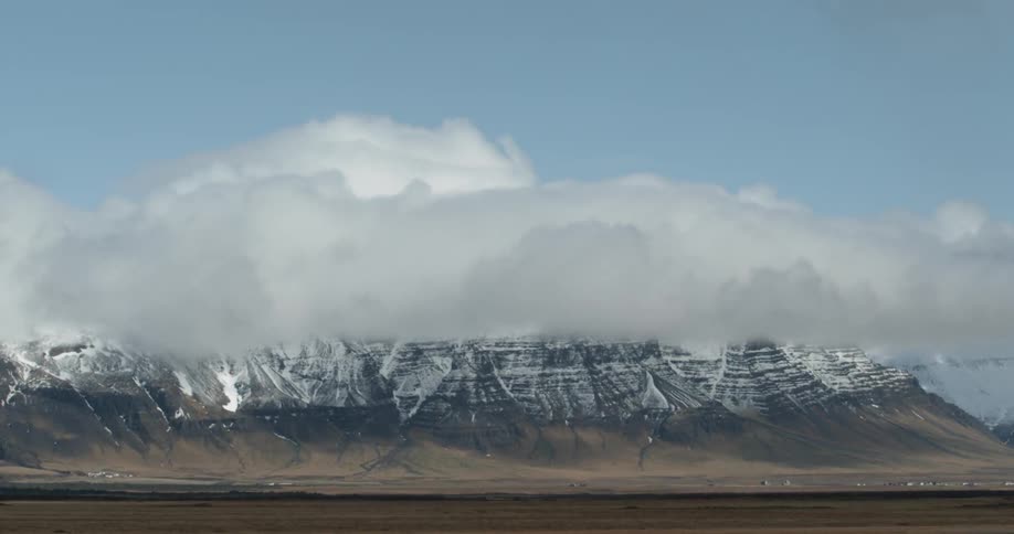 Thick white clouds are flowing over a snowy mountain range