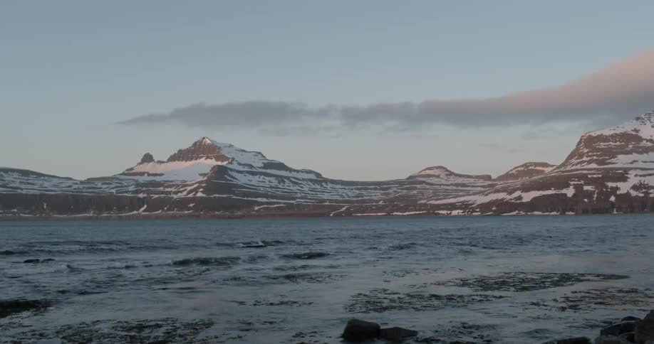 Ocean water flowing into bay and clouds forming over snowy mountains